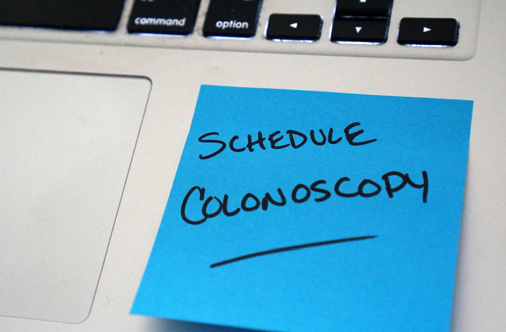 A note on a laptop that says Schedule Colonoscopy